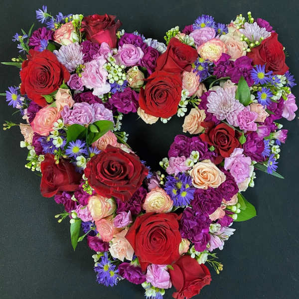 Heart-shaped bouquet of red, pink, and purple flowers on a dark background