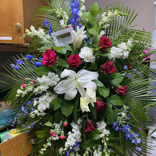 Large standing floral spray with red roses, white lilies, and blue flowers