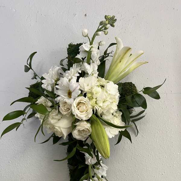 White lilies, roses, and daisies arranged on a moss-covered hanging cross.