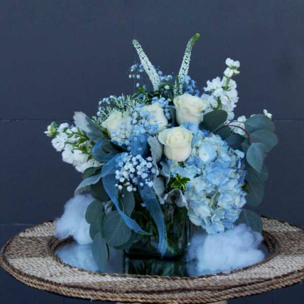 Blue and white floral arrangement in a glass vase on a woven tray