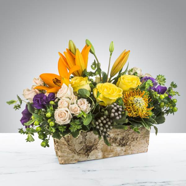 Mixed bouquet of lilies, roses, and purple blooms in a birch bark container