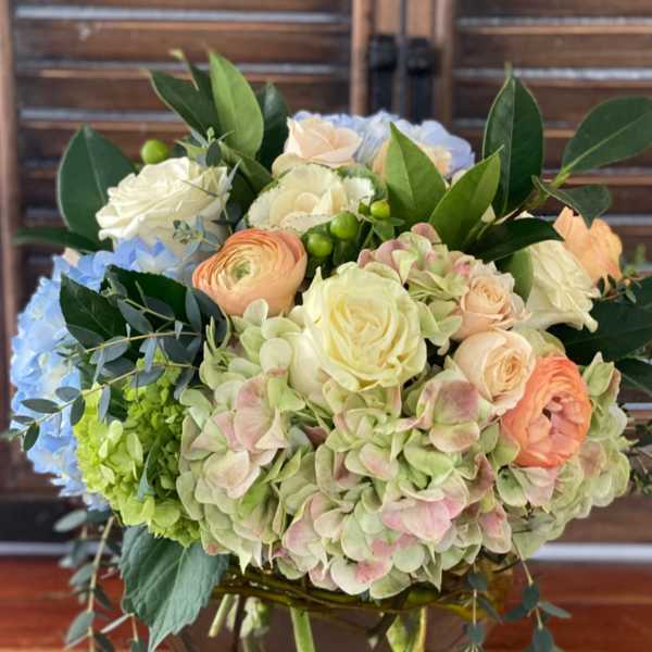 Mixed bouquet of pastel roses, hydrangeas, and ranunculus in a glass vase