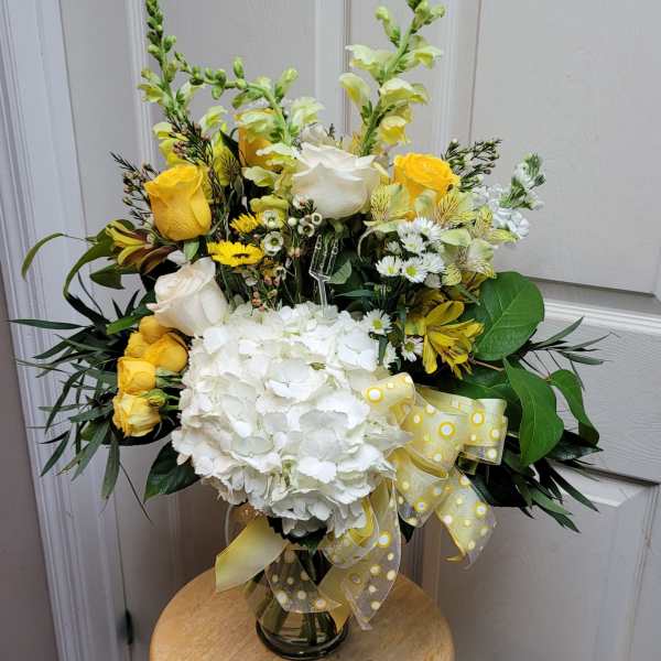 Yellow and white floral arrangement in a glass vase with a ribbon