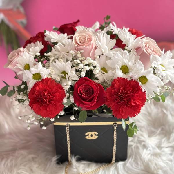 Red, pink, and white flowers arranged in a black gift box with gold chain detail