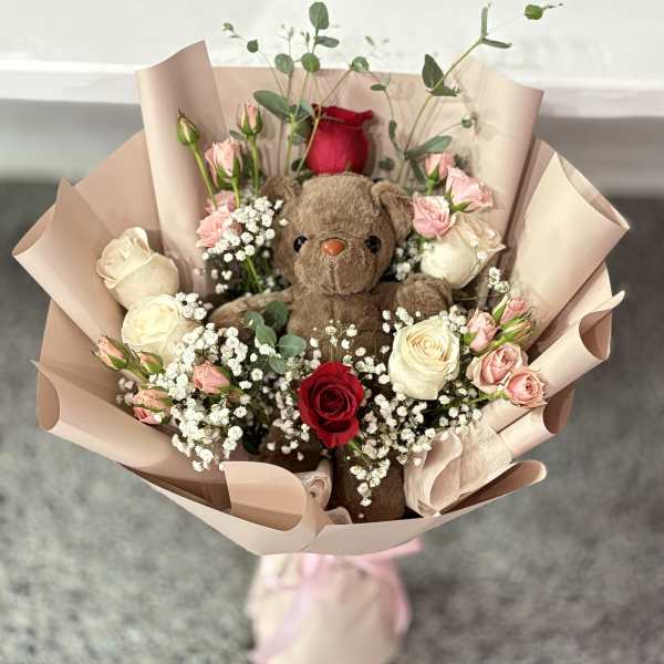 Bouquet with a teddy bear surrounded by roses and baby’s breath