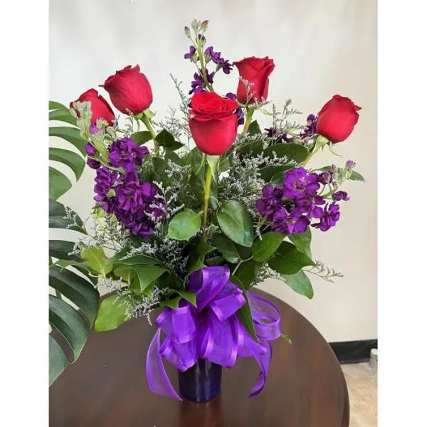 Bouquet of red roses and purple flowers in a vase with a purple ribbon