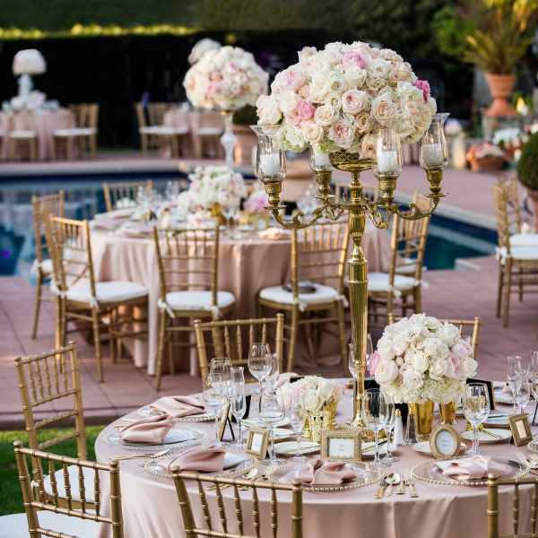 Blush and white rose centerpieces on gold stands at an outdoor table setting.