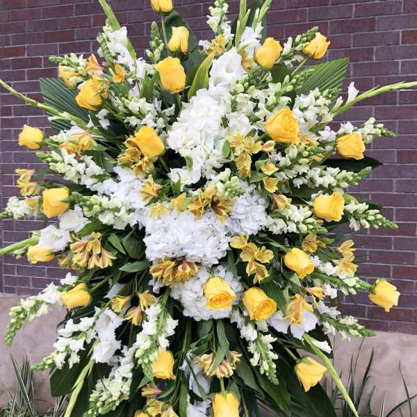 Tall standing spray of yellow roses, white hydrangeas, and white flowers on an easel