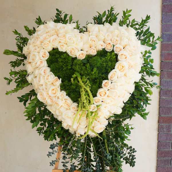 Heart-shaped white rose wreath on an easel with green foliage