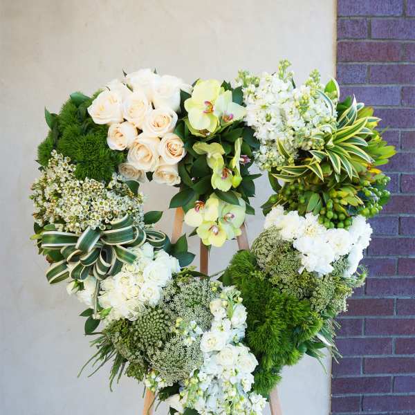 Heart-shaped floral wreath on a wooden easel with white and green flowers
