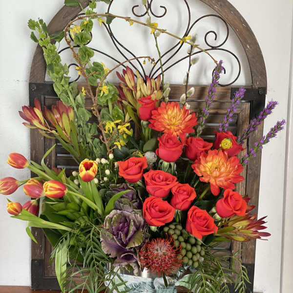 Mixed floral arrangement with red roses, orange dahlias, and tulips in a metal container