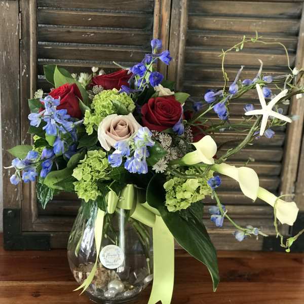 Bouquet of red and blush roses with blue flowers in a glass vase