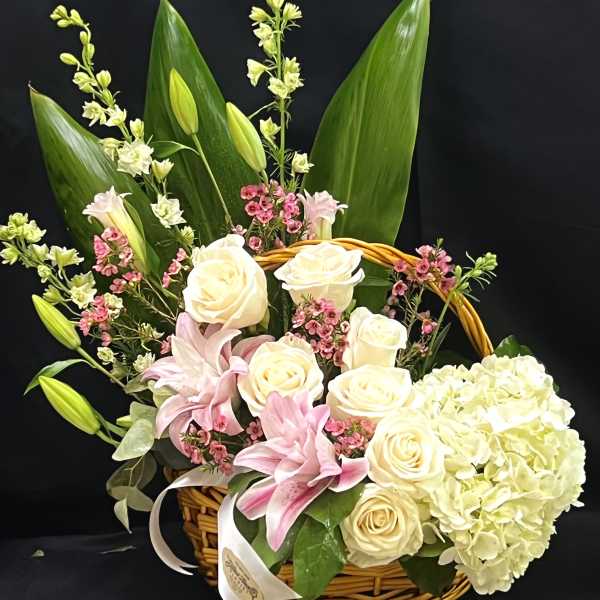 Basket arrangement of cream roses, pink lilies, and white hydrangea