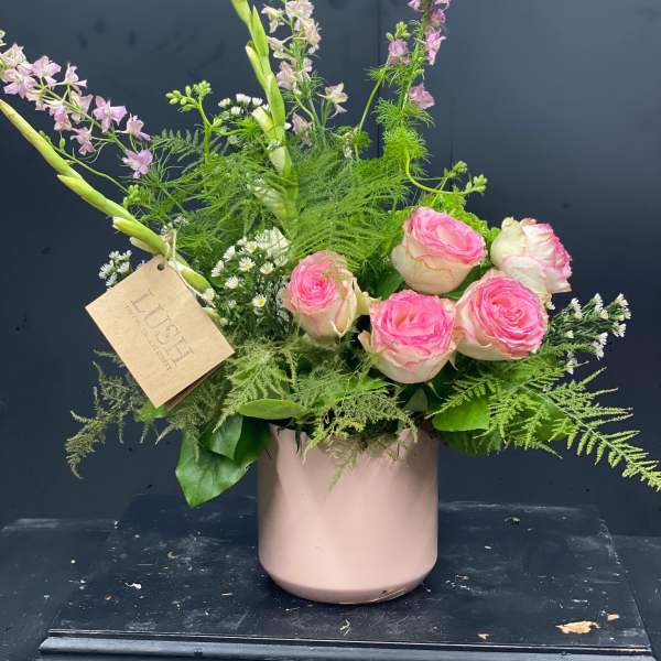 Pink roses and purple flowers arranged in a blush vase