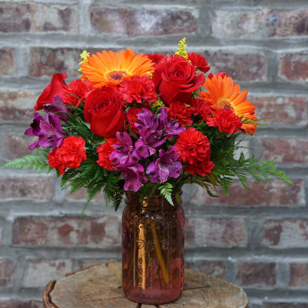 Bouquet of red roses, orange gerbera daisies, and purple flowers in a glass vase