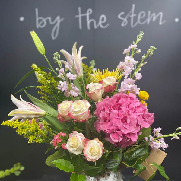 Mixed bouquet with pink hydrangea, roses, lilies, and yellow accents in a white vase