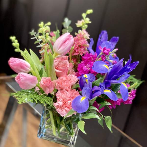 Pink tulips, roses, carnations, and purple irises in a glass vase