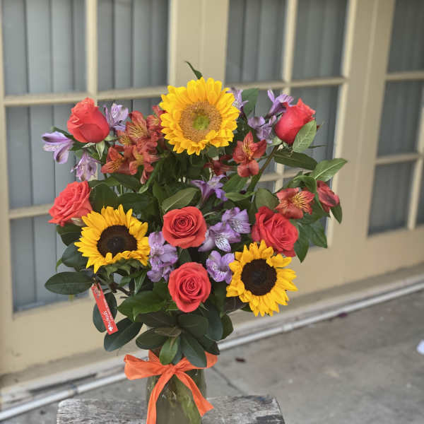 Bouquet of sunflowers, red roses, and purple alstroemeria in a glass vase