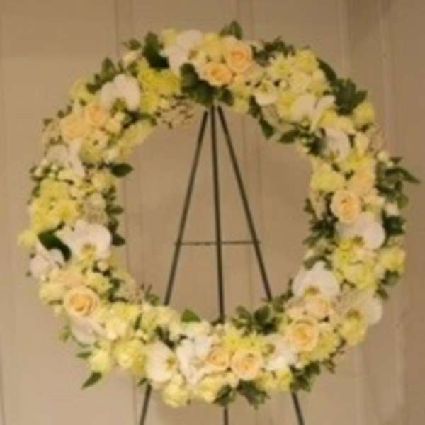Large floral wreath on a black easel with white and pale yellow flowers