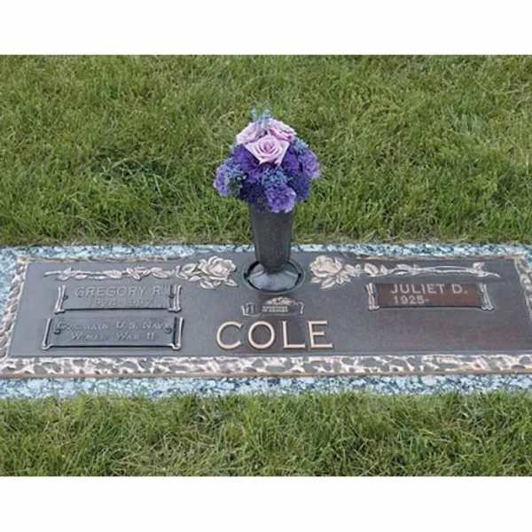 Purple floral arrangement in a cemetery vase on a grave marker