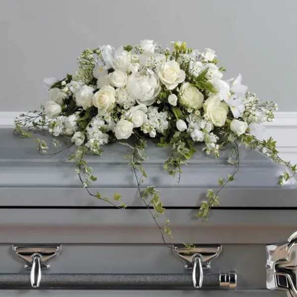White floral casket spray with trailing ivy on a gray casket