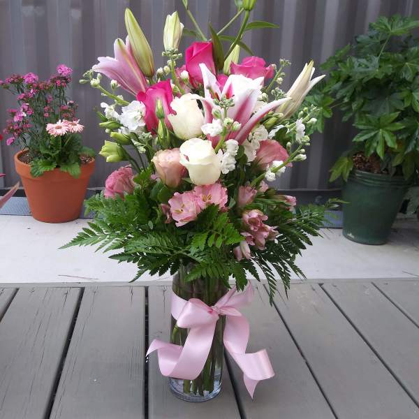 Pink and white lilies and roses in a glass vase with a pink ribbon