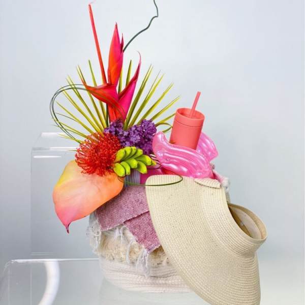 Bright tropical floral arrangement with a woven visor and pink cup