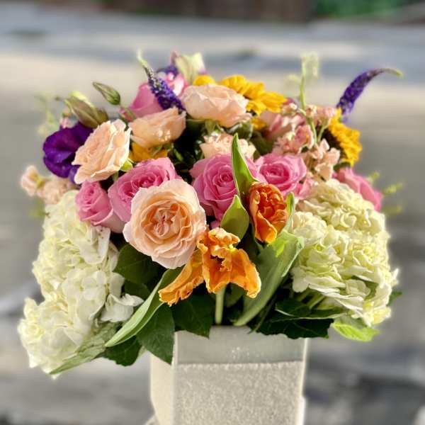 Mixed bouquet of pink, peach, purple, and yellow flowers in a square vase