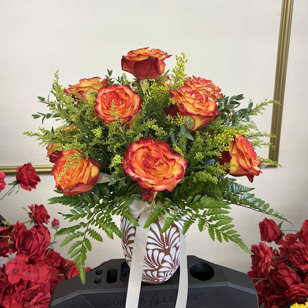 Orange-red roses in a patterned vase with a white ribbon