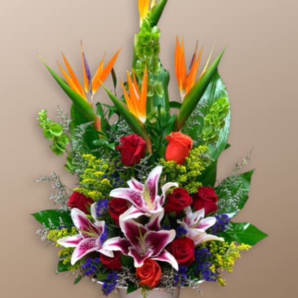 Tropical bouquet with red roses and pink lilies in a white container