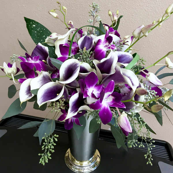 Purple and white calla lilies with orchids in a black vase