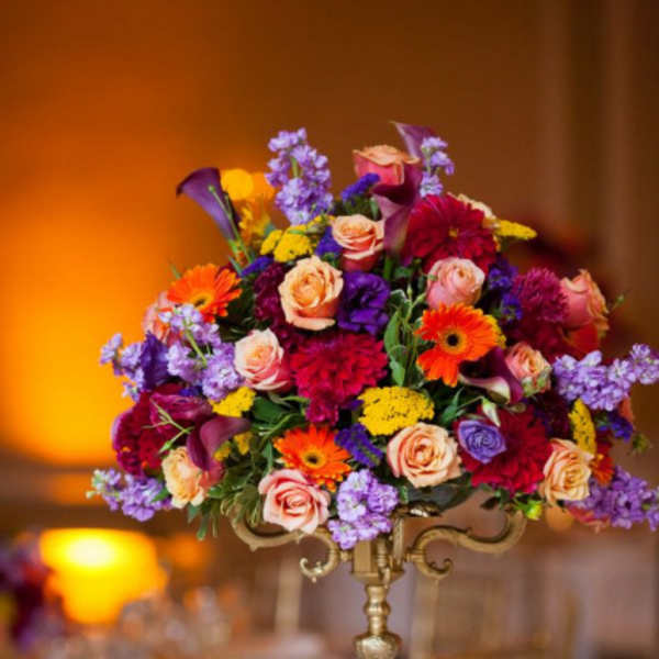 Tall floral centerpiece with roses, calla lilies, and gerbera daisies in a gold stand