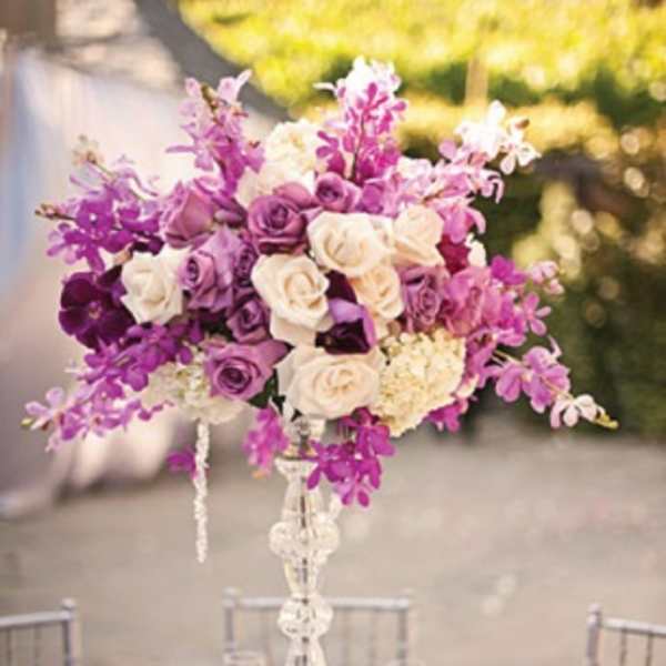Tall purple and white floral centerpiece on a clear stand