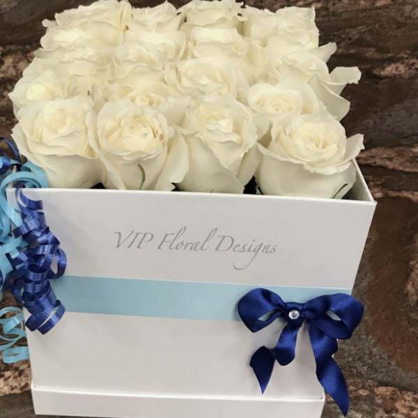 White roses arranged in a white gift box with blue ribbon accents.
