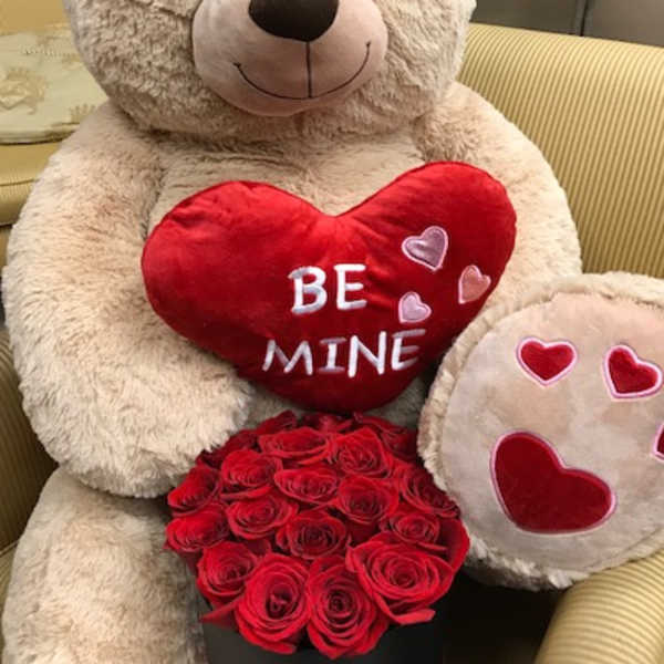 Large teddy bear holding a red heart pillow and a box of red roses