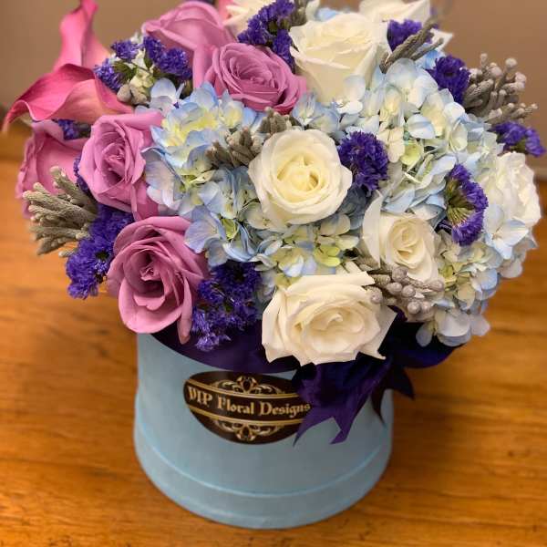 Bouquet of pink and white roses with blue hydrangeas in a round box