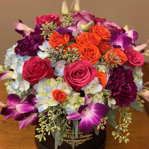 Round bouquet of pink, orange, and purple flowers in a black box