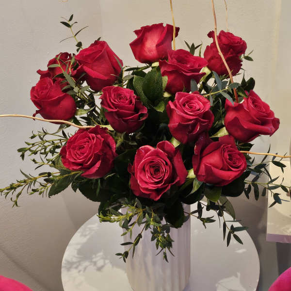 Red roses arranged in a white vase with greenery