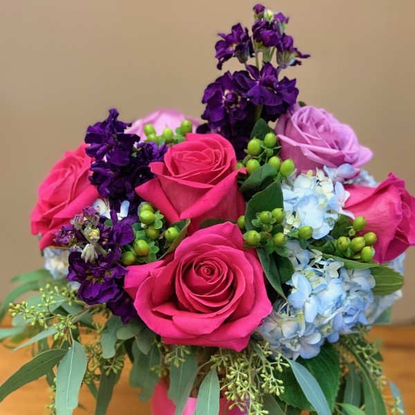 Bouquet of pink roses, purple blooms, and blue hydrangeas in a glass vase