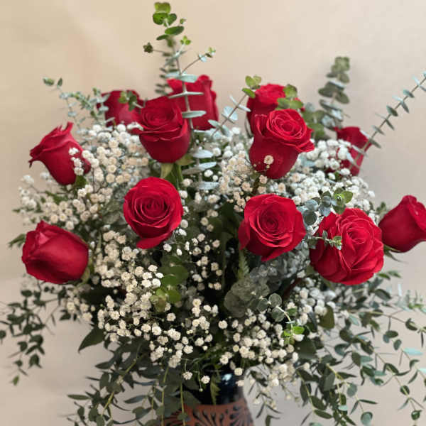 Red roses arranged in a decorative vase with baby's breath and eucalyptus