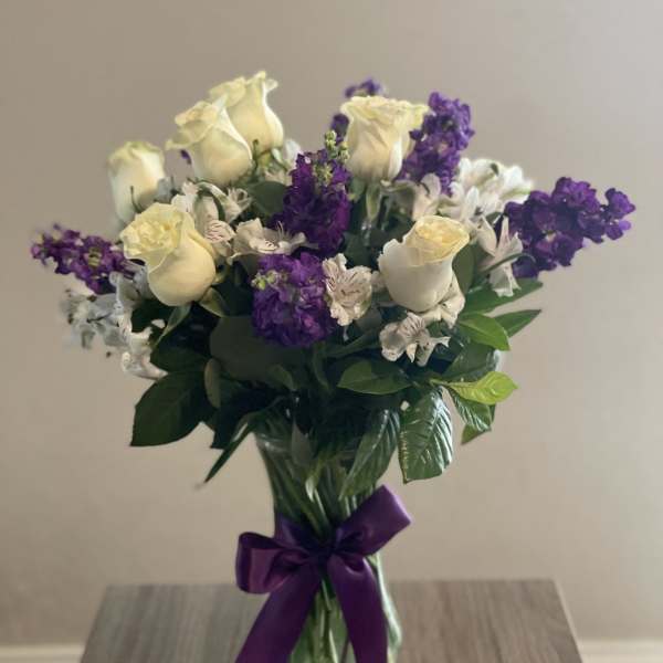 Bouquet of cream roses and purple flowers in a glass vase with a purple ribbon