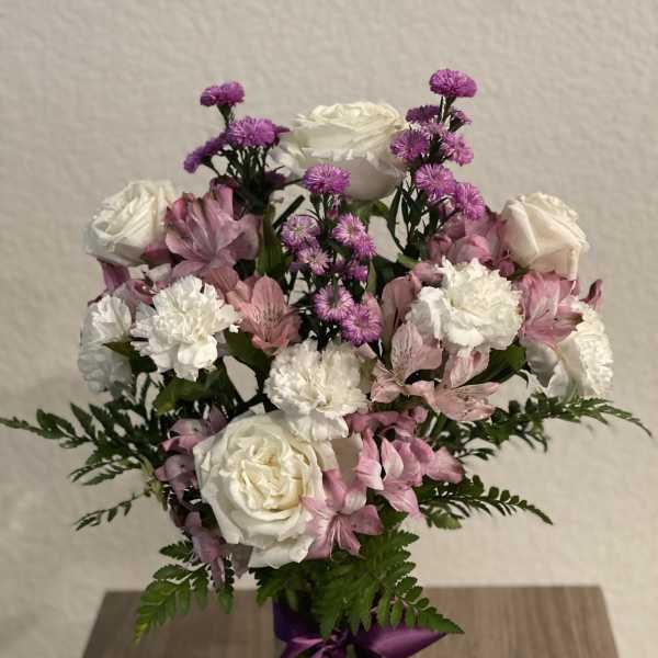 Pink and white bouquet in a glass vase with a purple ribbon