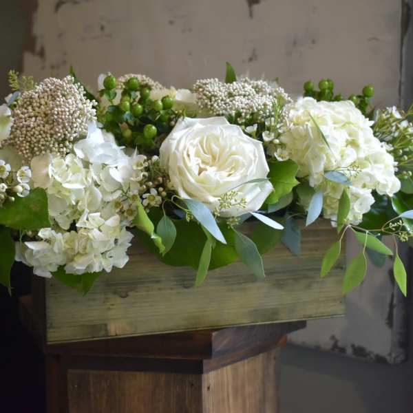 White floral arrangement in a wooden box with greenery