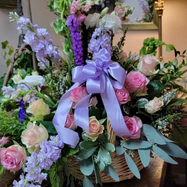 Basket arrangement of pink and lavender roses with a purple ribbon