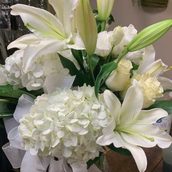 White lilies and hydrangeas in a clear glass vase with a white ribbon