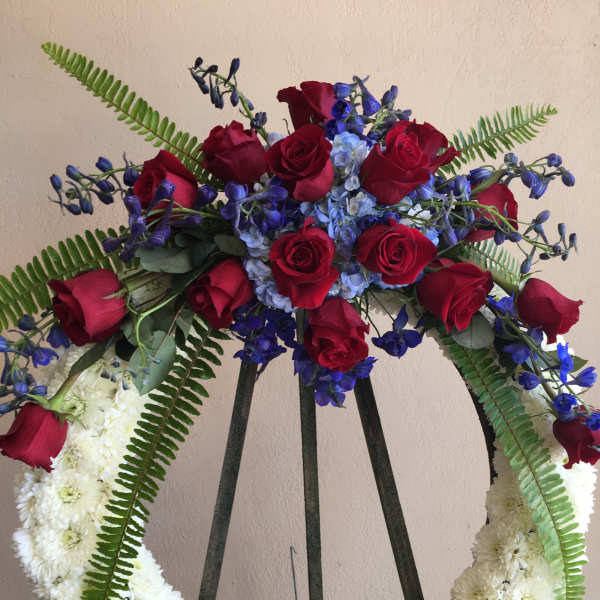 Heart-shaped floral wreath with red roses, blue flowers, and white chrysanthemums