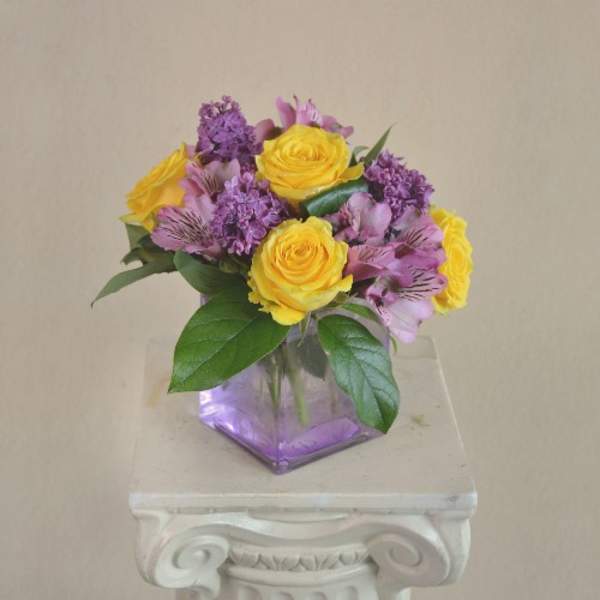 Yellow roses and purple flowers in a square glass vase
