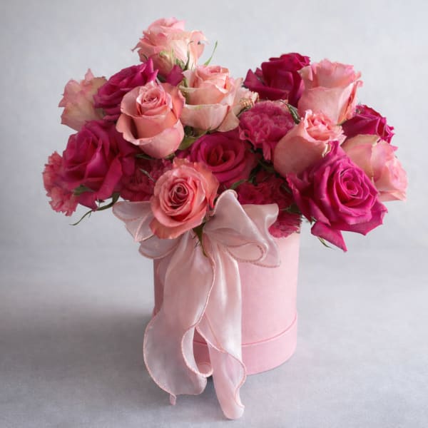 Pink and magenta roses arranged in a round pink box with a ribbon bow