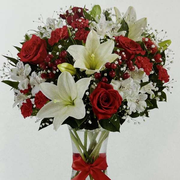 Red roses and white lilies in a clear glass vase with a red ribbon