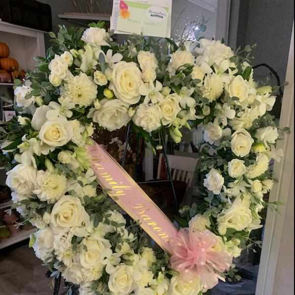 Heart-shaped white floral wreath with a pink ribbon and bow